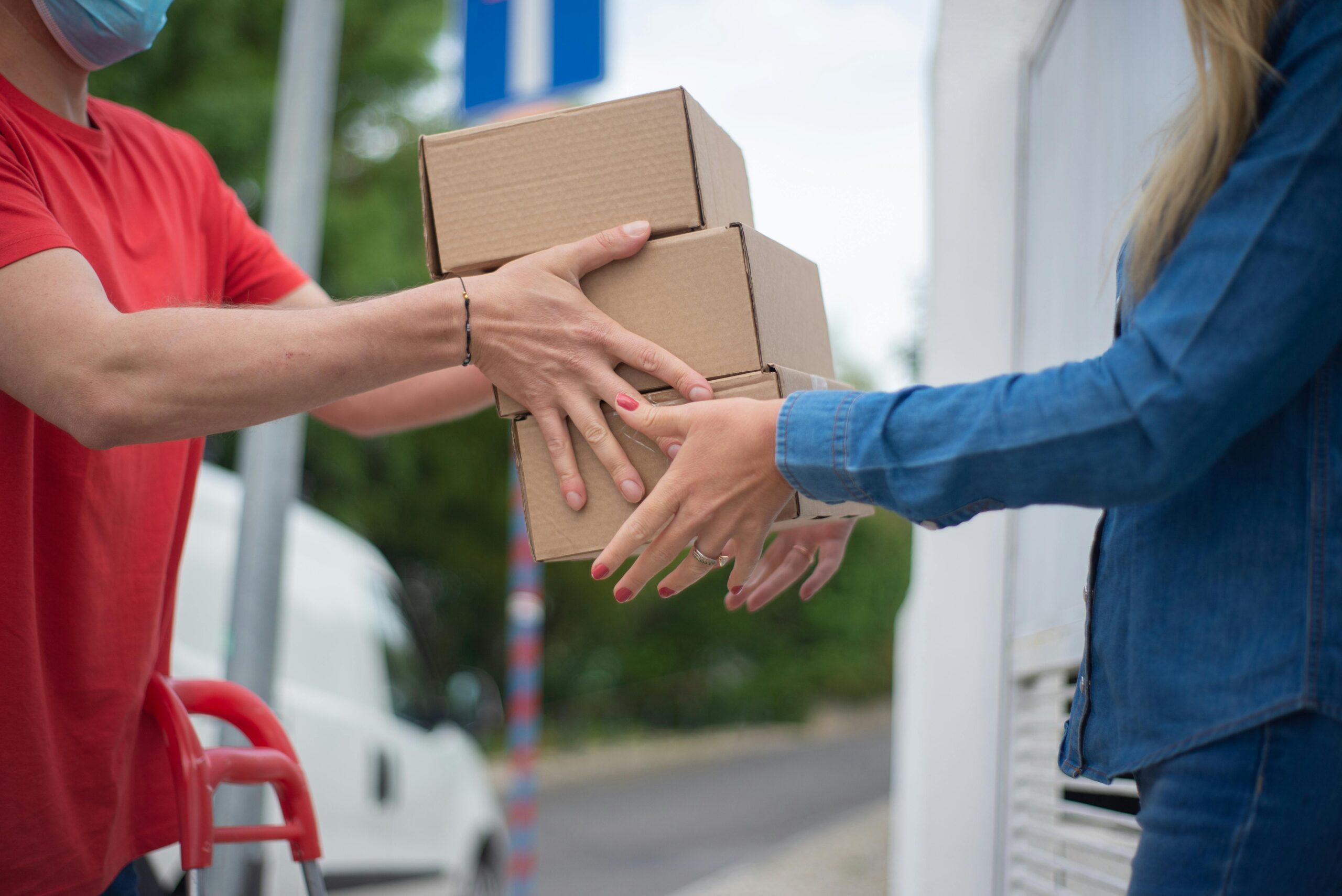 Hands exchanging cardboard boxes during an outdoor delivery scene.